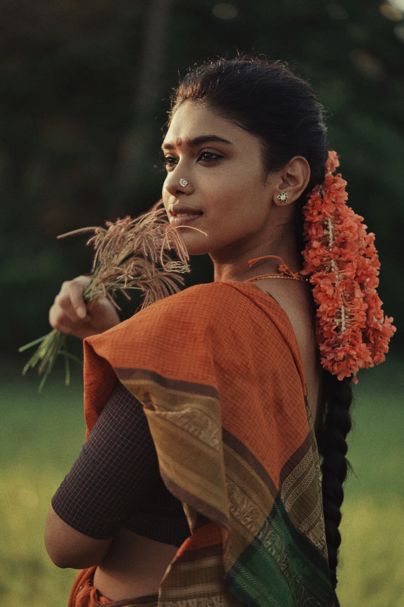 Portrait of a woman with a garland of orange flowers in her braid, a handloom saree draped over her shoulder